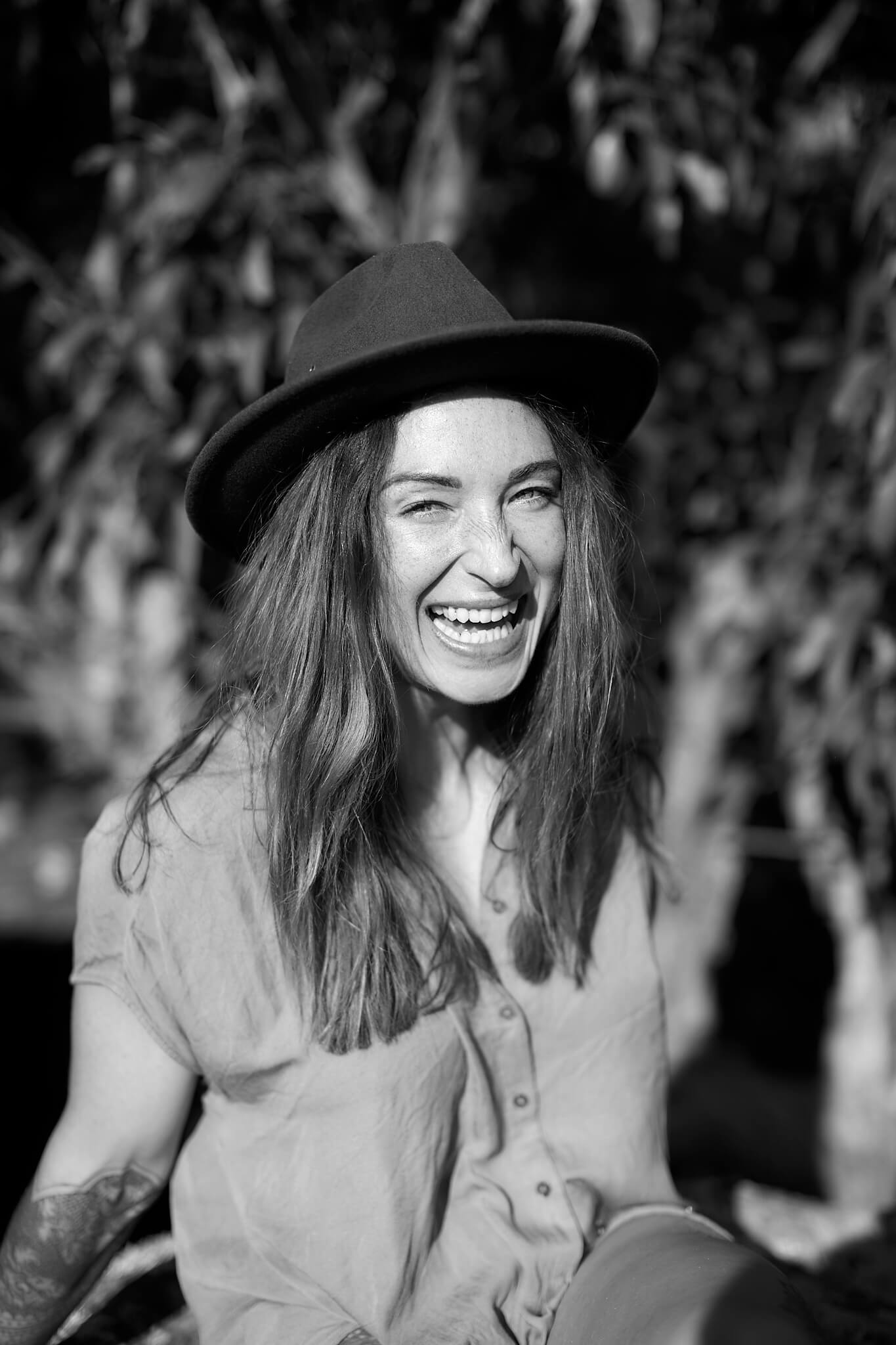 A woman laughing and smiling in the bush wearing a hat